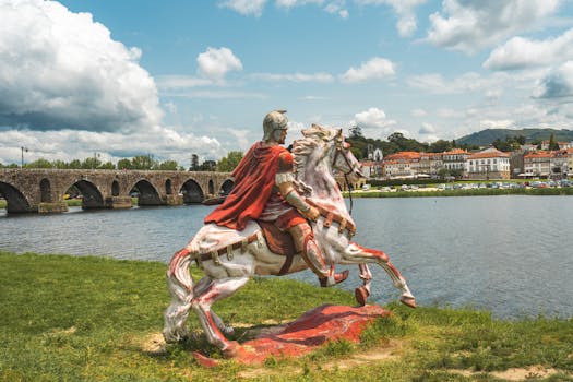 A striking statue of Roman cavalry with a scenic backdrop of Ponte de Lima and its iconic bridge in Portugal.