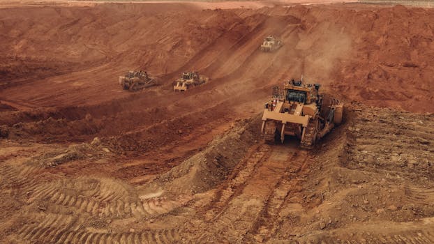 Aerial shot of heavy machinery at work in a Brazilian open pit mine with dusty red earth, depicting industrial operation.
