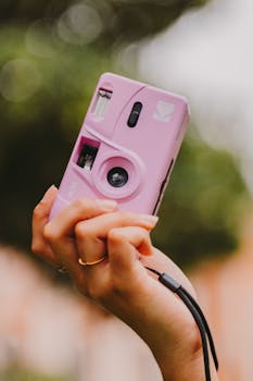 Hand holding a pink analog camera with bokeh background. Shot in Belém, Brazil.