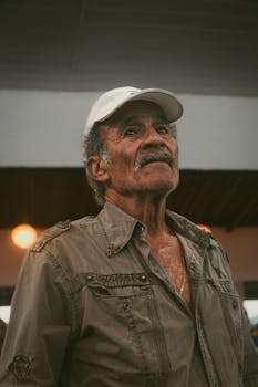 Portrait of an elderly man wearing a casual shirt and cap, set against an indoor backdrop.