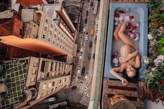 Pregnant woman in a bathtub with flowers, high above the city street, offering a unique urban bath experience.