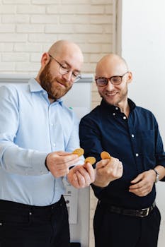 Two colleagues smiling and examining cryptocurrency coins in a modern office setting.